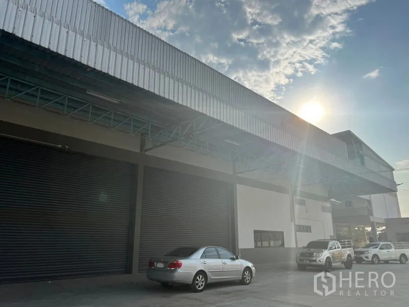 Warehouse for rent in Lat Krabang, Bangkok - Front facade of the warehouse with several large roller shutters, parking area and afternoon sun.