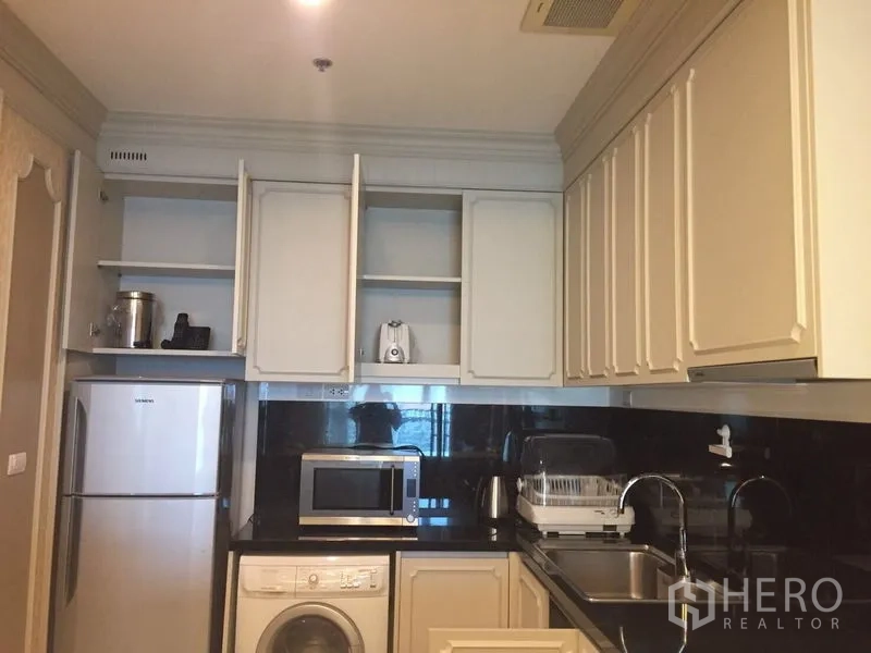 公寓 出租在Khlong Toei, Bangkok - 紧凑厨房，白色橱柜与黑色防溅板，配备冰箱、微波炉和洗衣机。