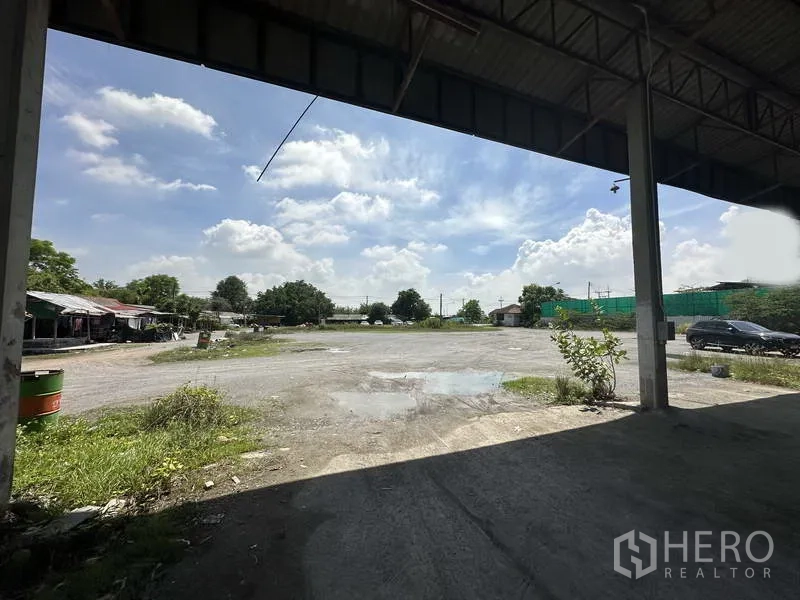 โรงงาน ให้เช่าในPhra Nakhon Si Ayutthaya - มุมมองจากใต้หลังคาไปยังลานกรวดโล่ง ใกล้ประตูทางเข้าและแนวต้นไม้