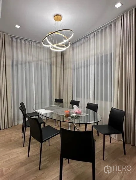 Detached House for rent - Dining corner with a round glass table, six black chairs and a ring pendant light.