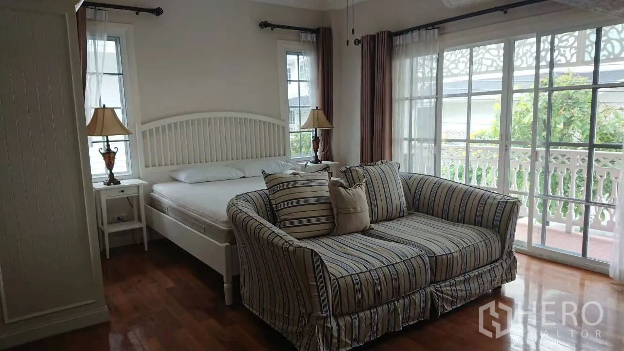 Detached House for rent in Mueang Samut Prakan, Samut Prakan - Master bedroom with balcony access, striped loveseat and floor-to-ceiling windows.