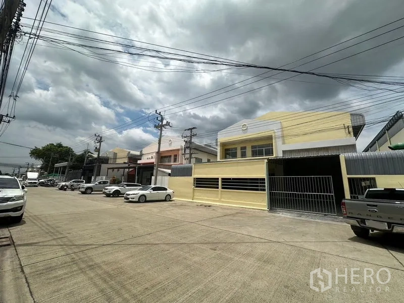Factory for rent in Pathum Thani - Row of factory buildings with gated fronts on a wide concrete road in Khlong Luang, Pathum Thani.