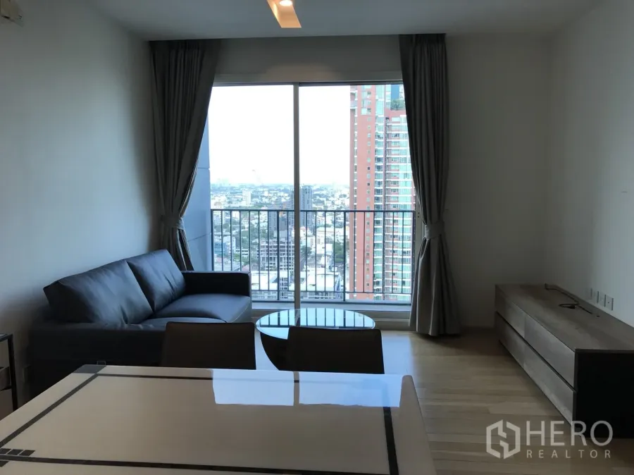 Condominium for rent in Khlong Toei, Bangkok - Bright living room with sofa, dining area and balcony opening to a Bangkok skyline view.