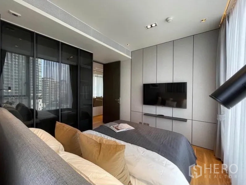 Condominium for rent in Khlong Toei, Bangkok - Bedroom featuring built-in wall panels, mounted TV and glass wardrobe doors.