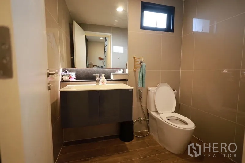 Detached House for rent or sale in Lam Luk Ka, Pathum Thani - Modern bathroom with vanity, mirror and toilet in neutral tiles.