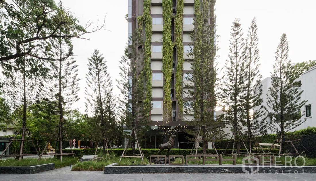 Condominium for rent in Khlong Toei, Bangkok - Condominium entrance with landscaped garden and tall trees in Khlong Toei.