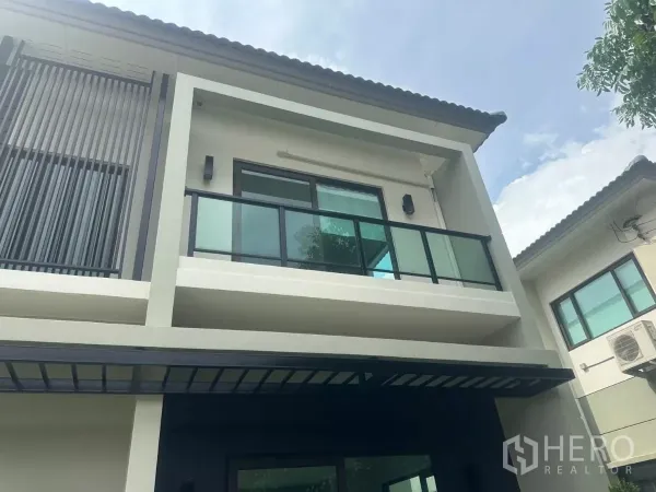 独立式住宅 出售在Samut Prakan - 上层立面特写，可见玻璃阳台与竖向格栅及屋檐。