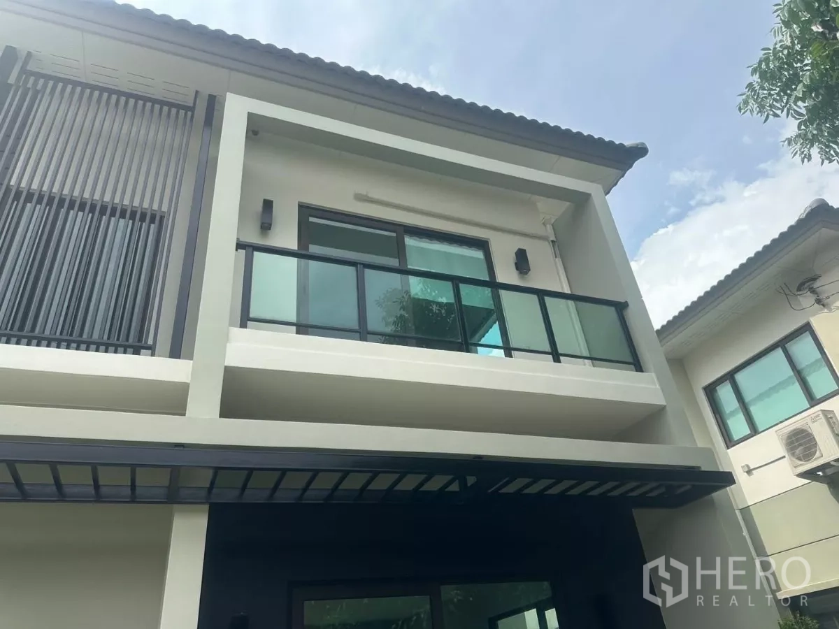 独立式住宅 出售在Samut Prakan - 上层立面特写，可见玻璃阳台与竖向格栅及屋檐。