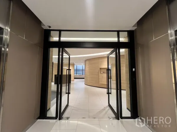 Office Space for rent in Huai Khwang, Bangkok - Glass double doors opening to a modern office lobby with wood walls and white tiles.