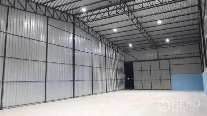 货栈 出租在Pak Kret, Nonthaburi - 仓库内部空间开阔，钢桁架高挑屋顶，LED照明明亮，混凝土地面平整。