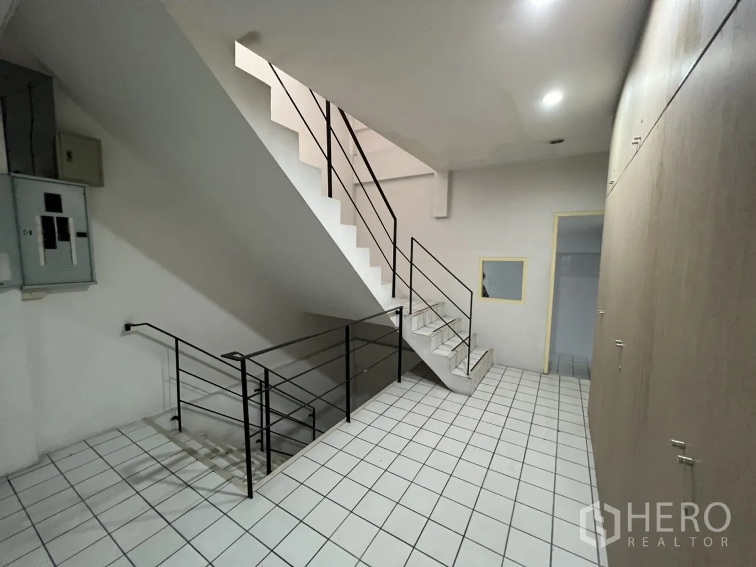 Shophouse for rent or sale in Watthana, Bangkok - Stair landing with storage wall and white tiled flooring.