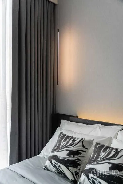 Condominium for rent in Watthana, Bangkok - Bedroom corner with layered gray curtains, bedside lighting, and patterned pillows.