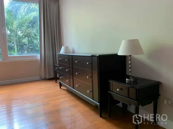 คอนโด ให้เช่าในPathum Wan, Bangkok - มุมห้องนอนพร้อมตู้ลิ้นชักสีดำ โต๊ะข้าง และโคมไฟข้างหน้าต่าง