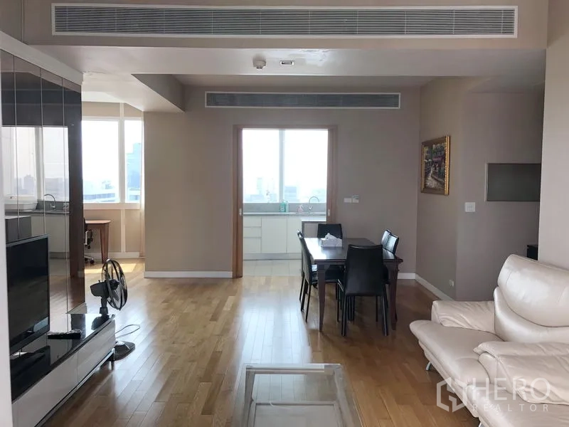 Condominium for rent in Khlong Toei, Bangkok - Open-plan lounge with dining table and doorway to a separate kitchen with a large window.
