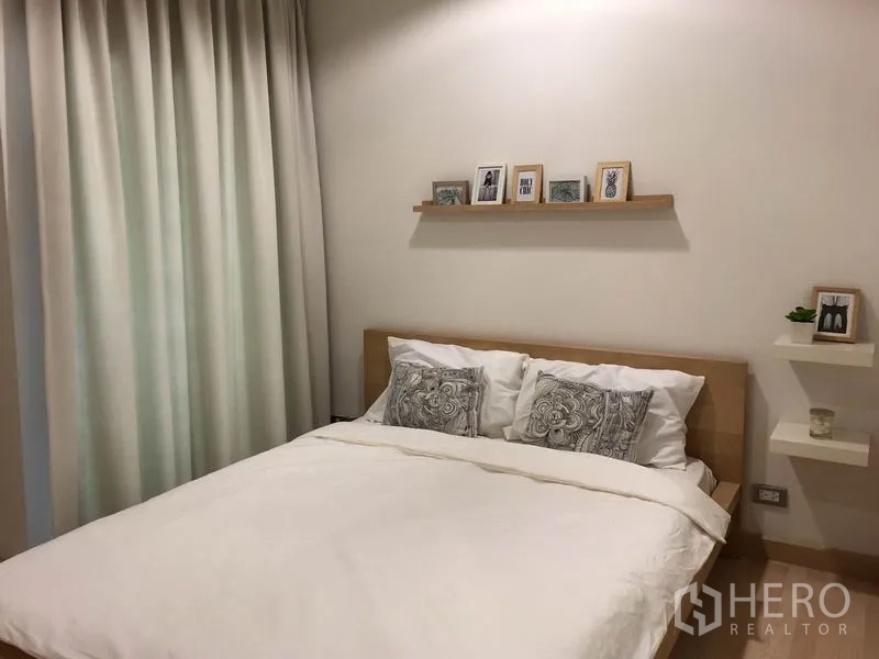 公寓 出租或出售在Watthana, Bangkok - 极简卧室细节，床铺配花纹抱枕，旁有悬空置物架与长窗帘。