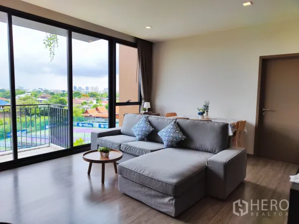 公寓 出租在Watthana, Bangkok - 采光充足的客厅，落地窗与阳台，俯瞰网球场与绿意景观。