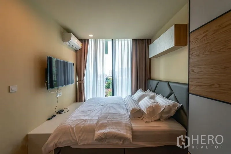 公寓 出租在Watthana, Bangkok - 卧室采光充足，落地窗、墙挂电视与软包床头。