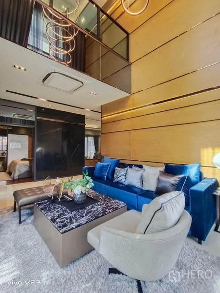 独立式住宅 出售在Wang Thonglang, Bangkok - 挑高客厅，蓝色天鹅绒沙发、大理石茶几与装饰吊灯。