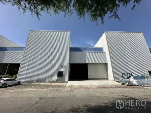 โรงงาน ให้เช่าในKhlong Luang, Pathum Thani - ด้านหน้าตัวอาคารโรงงานผนังเมทัลชีท ประตูม้วนขนาดใหญ่ และลานจอดรถ