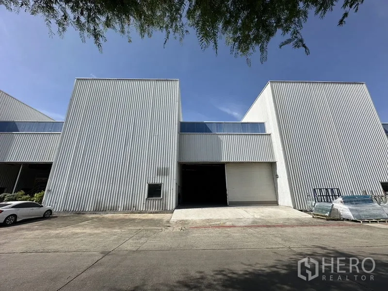 โรงงาน ให้เช่าในKhlong Luang, Pathum Thani - ด้านหน้าตัวอาคารโรงงานผนังเมทัลชีท ประตูม้วนขนาดใหญ่ และลานจอดรถ
