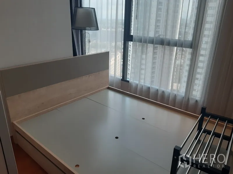 Condominium for rent in Khlong Toei, Bangkok - Bedroom with minimalist headboard, tall curtains and floor-to-ceiling window.