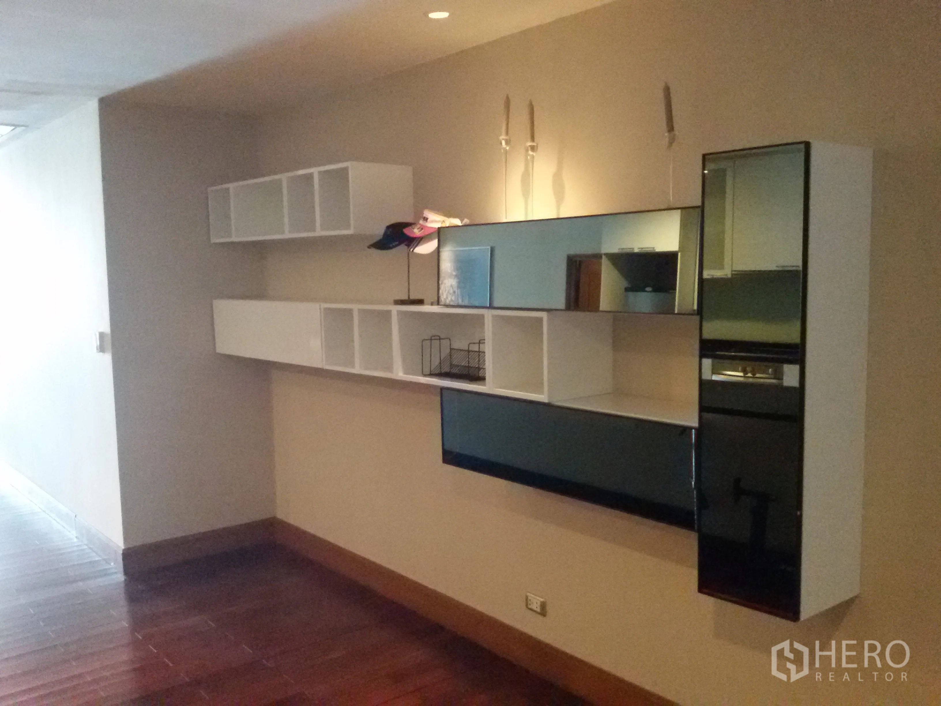 Condominium for rent in Sathon, Bangkok - Living area wall with floating shelves and mirrored cabinet over polished wooden floor.