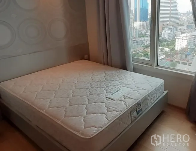 Condominium for rent in Khlong Toei, Bangkok - Second bedroom with big window, city view and soft neutral decor.