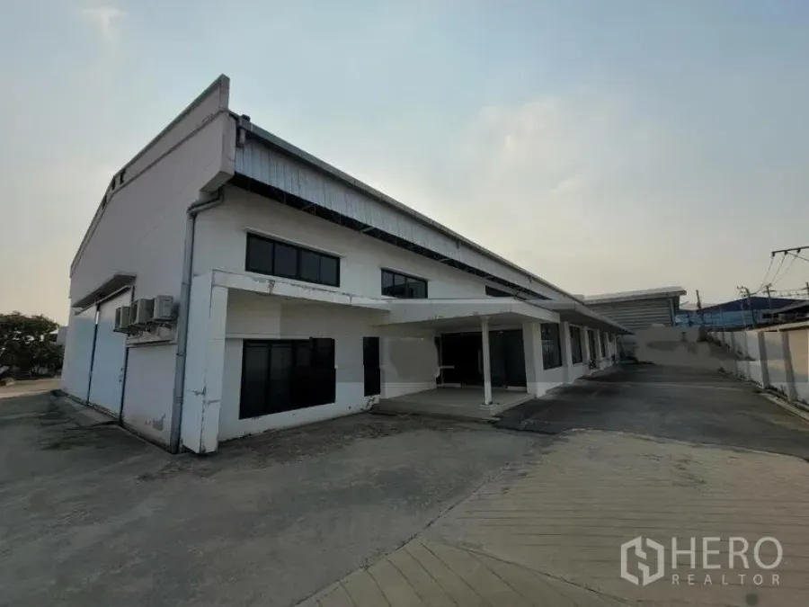 Factory for rent or sale in Prawet, Bangkok - Front exterior of a white factory building with a covered entry and wide driveway.