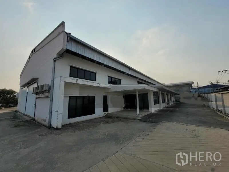 Factory for rent or sale in Prawet, Bangkok - Front exterior of a white factory building with a covered entry and wide driveway.