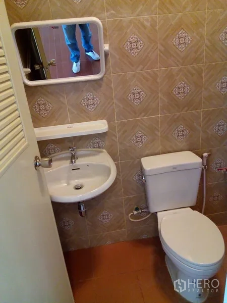 Shophouse for rent in Phra Khanong, Bangkok - Bathroom with sink, toilet and wall mirror on patterned tiles.