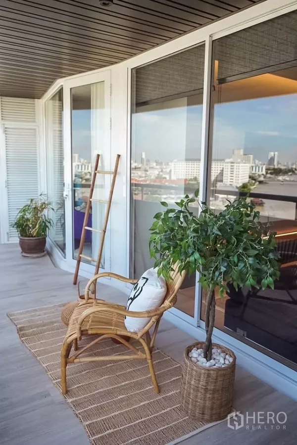 公寓 出租在Bang Phlat, Bangkok - 阳台近景：藤椅与盆栽，旁为整面落地玻璃门。