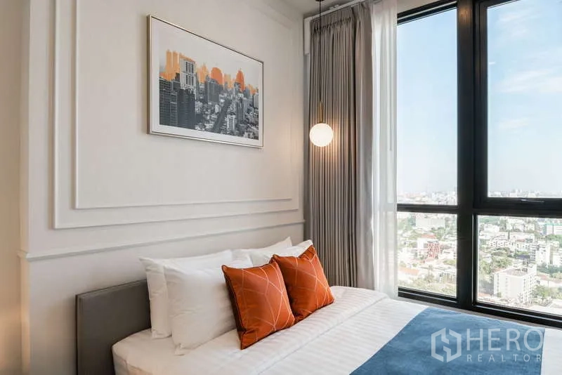 คอนโด ให้เช่าในWatthana, Bangkok - มุมใกล้เตียงพร้อมหมอนสีส้มและหน้าต่างบานใหญ่เห็นวิวกรุงเทพฯ