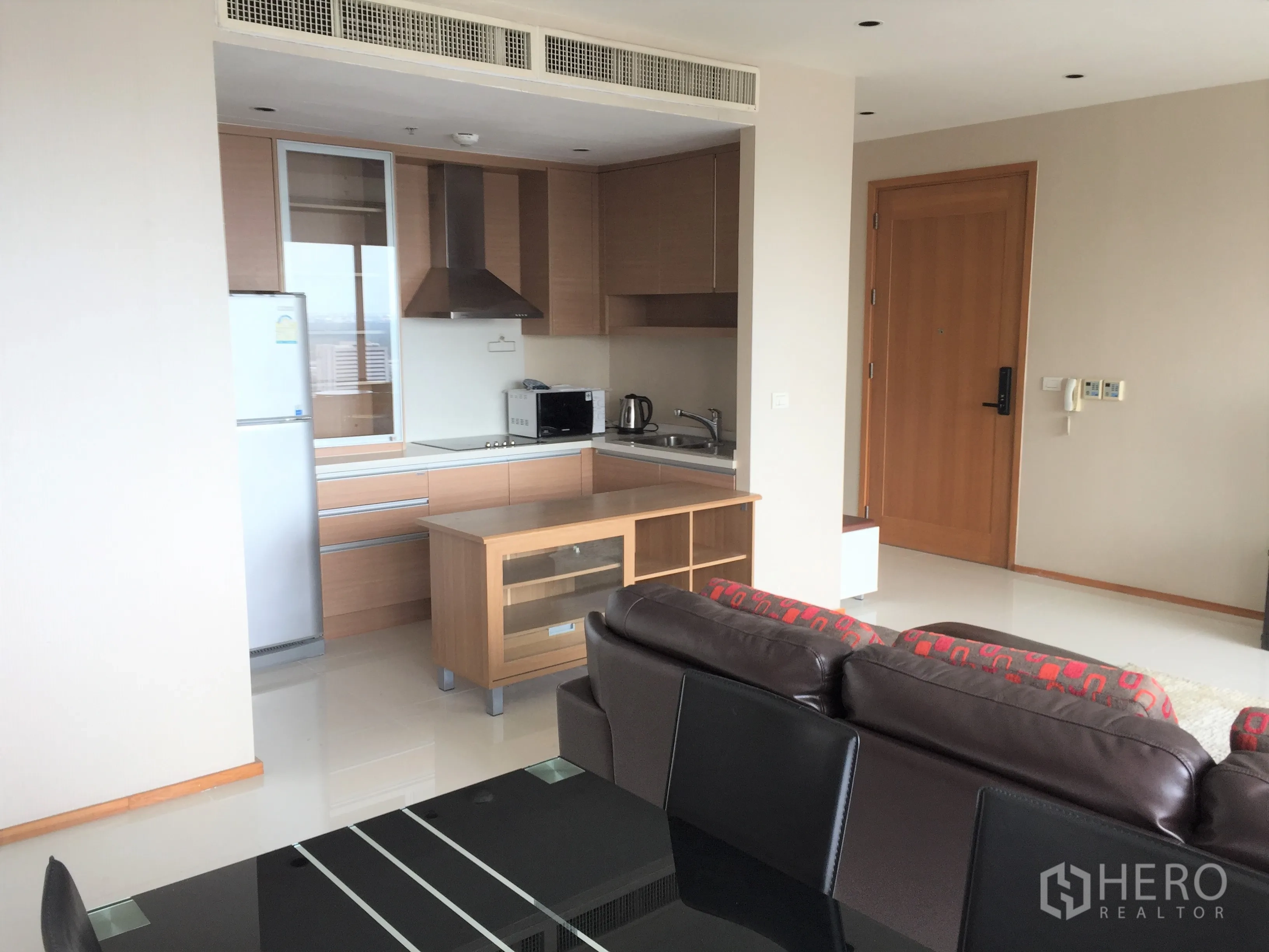 Condominium for rent or sale in Khlong Toei, Bangkok - Open-plan living and dining area with modern kitchenette, appliances, and light wood cabinetry.