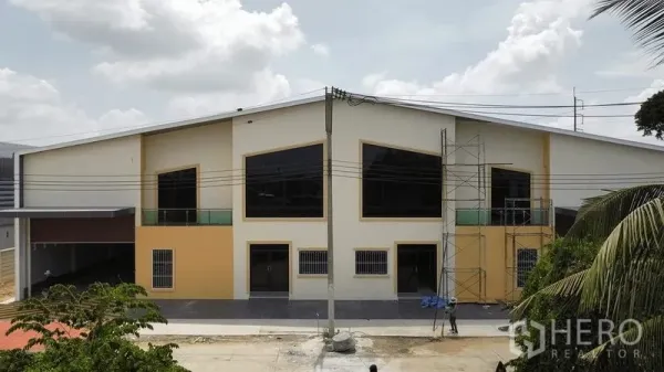 货栈 出租在Bang Pakong, Chachoengsao - 现代化仓库外立面，大片黑框玻璃窗，脚手架与宽阔车道。