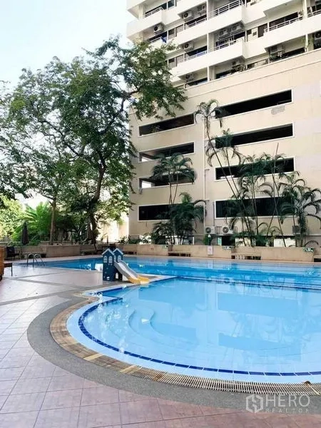 Condominium for rent or sale in Khlong Toei, Bangkok - Outdoor swimming pool with sundeck, trees and the condominium facade in Khlong Toei.