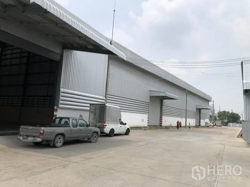 货栈 出租在Pathum Thani - 芭吞他尼大型金属板仓库外观，设多处装卸口与宽阔混凝土车道。