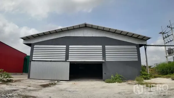คลังสินค้า ให้เช่าในChachoengsao - มุมหน้าของโกดังสีเทา ผนังเมทัลชีทลูฟเวอร์ ประตูบานเลื่อนขนาดใหญ่ และลานคอนกรีต