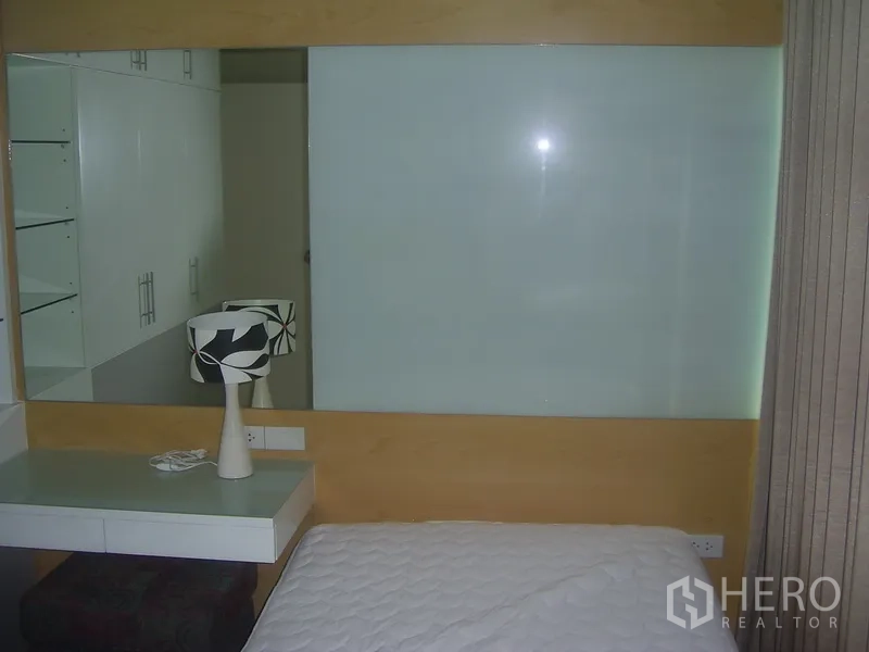 Condominium for rent in Khlong Toei, Bangkok - Compact bedroom corner with frosted glass panel, desk, and curtains.