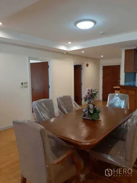 Apartment for rent in Watthana, Bangkok - Dining area with a six-seat wooden table, recessed lighting, and entryway beside the semi-open kitchen.