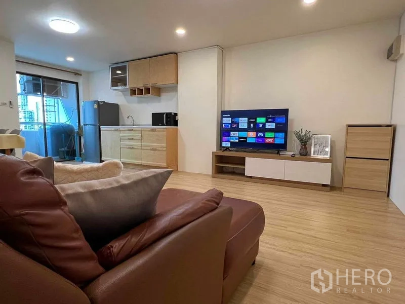 公寓 出租在Ratchathewi, Bangkok - 客厅内皮沙发对着智能电视，极简厨房，玻璃门连接阳台。