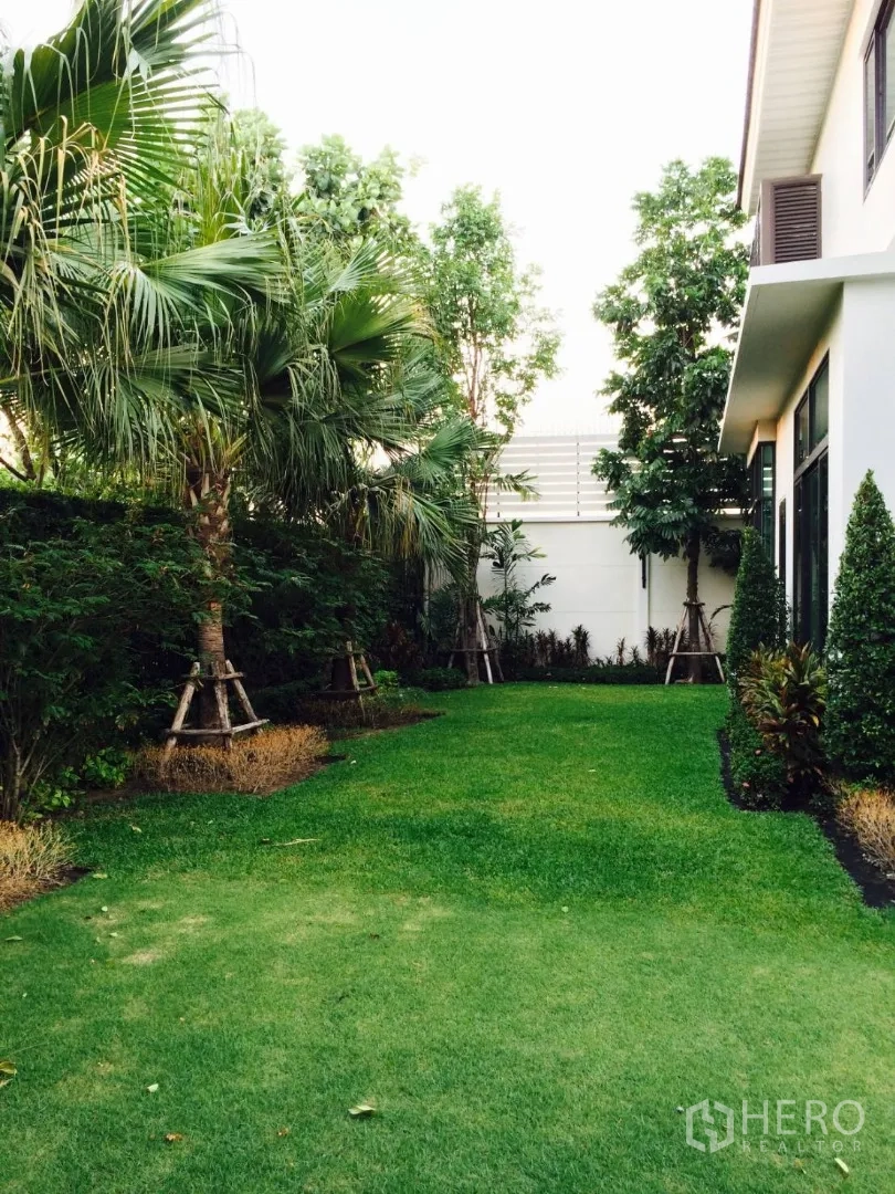 Detached House for sale in Lat Krabang, Bangkok - Shaded backyard lawn bordered by tropical trees beside the house.