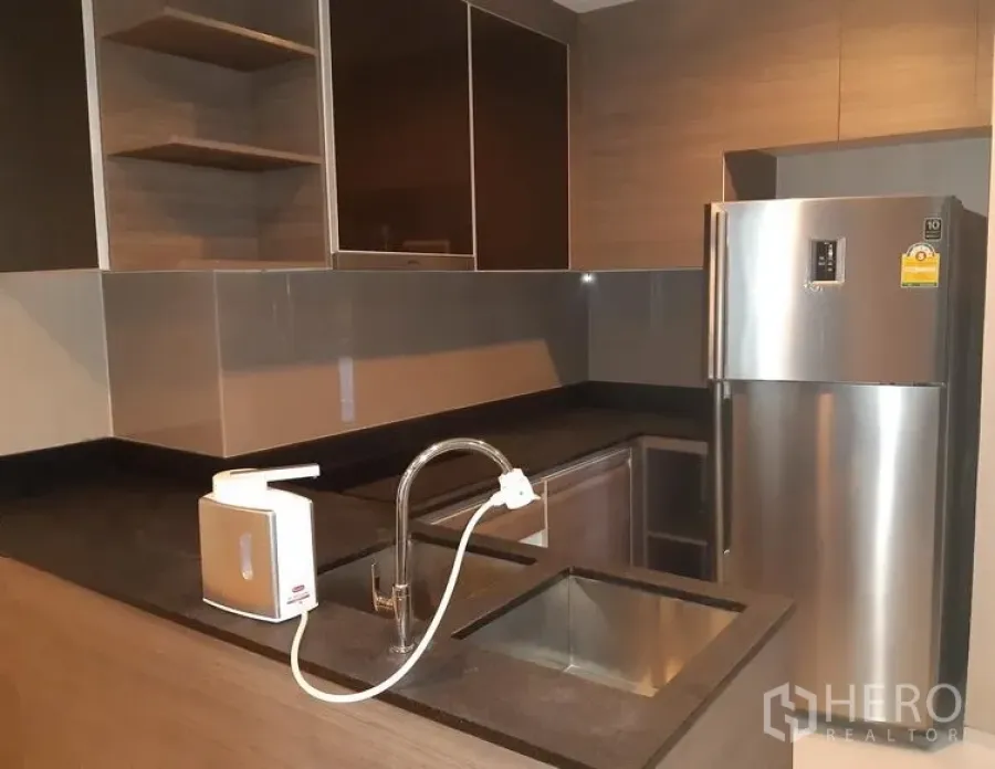 Condominium for rent in Khlong Toei, Bangkok - Modern condo kitchen with dark stone countertop, stainless sink, and large fridge.