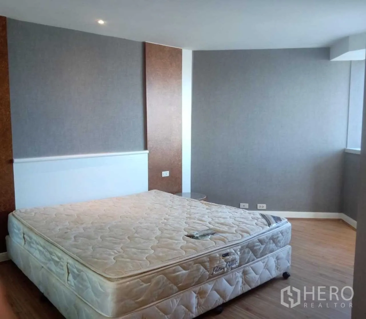 Condominium for rent in Khlong Toei, Bangkok - Bedroom with grey accent walls, wood flooring and a king-size mattress.