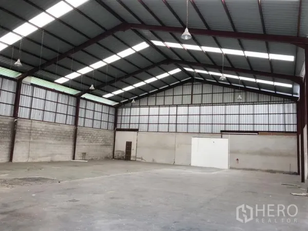 Warehouse for rent in Bueng Kum, Bangkok - Spacious warehouse interior featuring a high steel truss roof, skylights, concrete floor, and hanging lights.