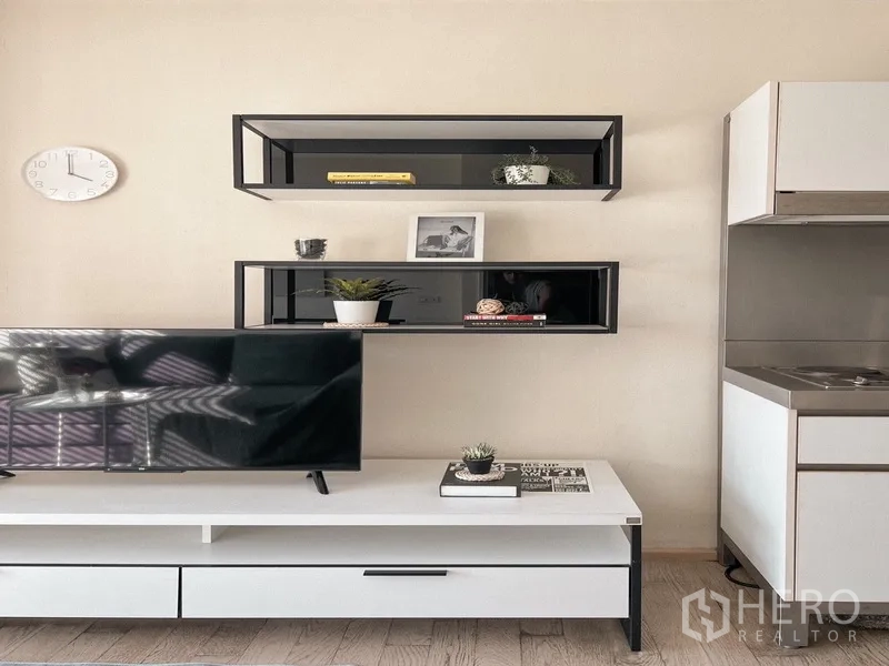 Condominium for rent in Khlong Toei, Bangkok - Media wall with floating shelves, flat‑screen TV, and a glimpse of the compact kitchenette.
