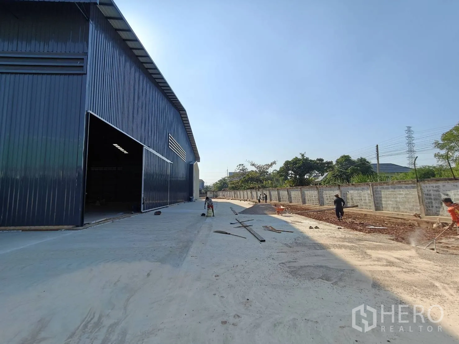 โรงงาน for rent in Mueang Samut Sakhon, Samut Sakhon - อาคารโรงงานผนังเมทัลชีทพร้อมประตูสไลด์ขนาดใหญ่และถนนคอนกรีตกว้างข้างกำแพงรั้ว.