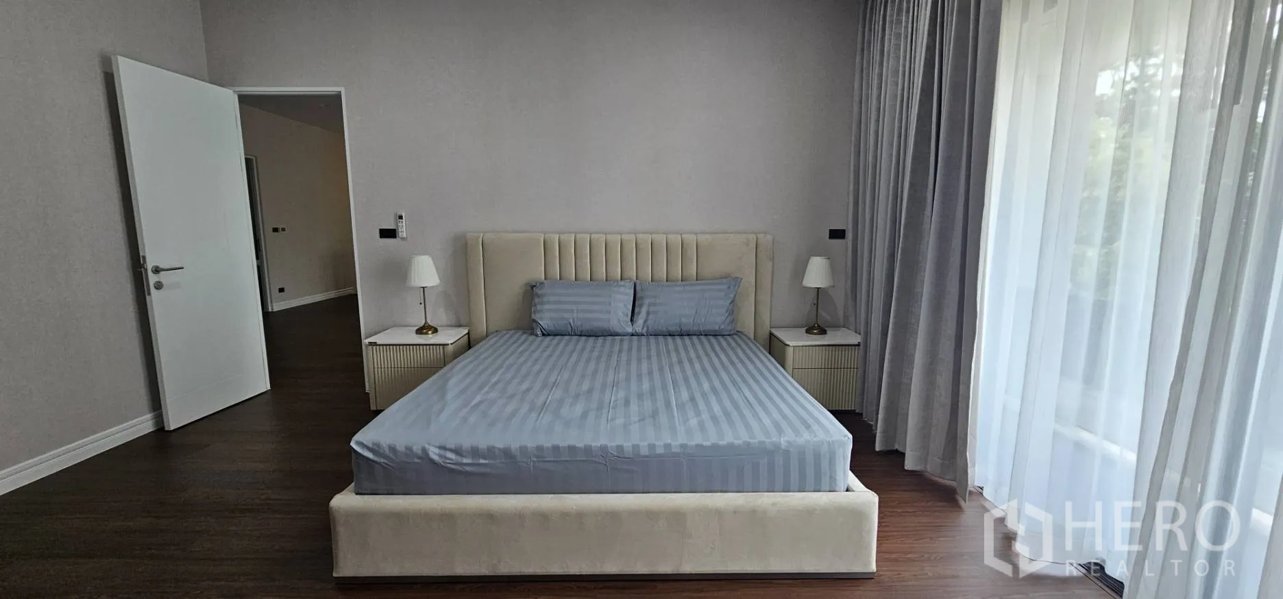 Detached House for rent in Bang Kapi, Bangkok - Master bedroom with upholstered bed and curtain-lined balcony doors.