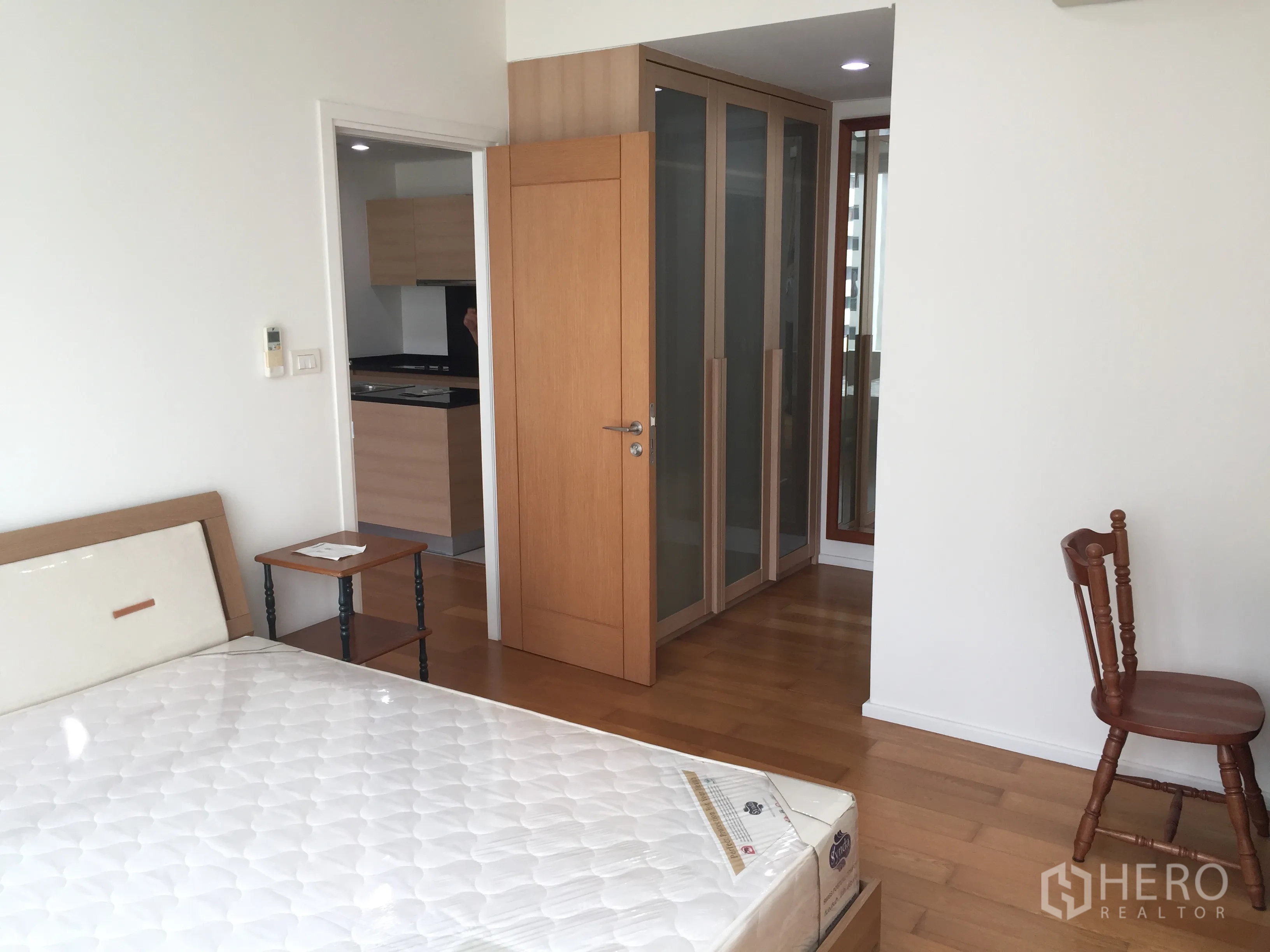 公寓 出租或出售在Watthana, Bangkok - 卧室设嵌入式衣柜与木地板，门通向厨房区域。