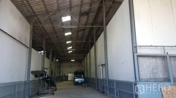 Warehouse for rent in Pathum Thani - Covered loading bay with steel trusses, ramp access, and trucks inside the warehouse.