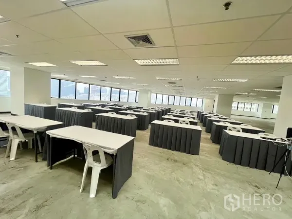 Office Space for rent - Bright office floor set up with rows of training tables and chairs beside panoramic city-view windows.